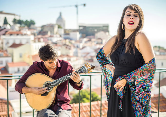 A Fado singer and guitarist performing on a balcony with Lisbon, Portugal blurred in the background