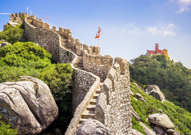 The Moorish Castle wall with flags and in the back ground the Palace of Pena in Portugal